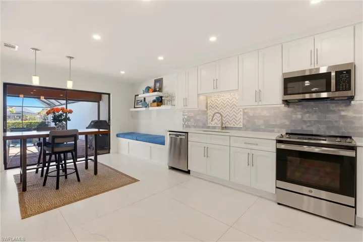 Kitchen featuring stainless steel appliances, white cabinetry, hanging light fixtures, and open shelves