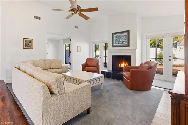 Living area featuring french doors, a high ceiling, a fireplace, a ceiling fan, and wood finished floors