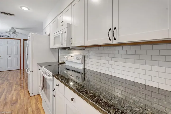 Kitchen with light wood-style flooring, a ceiling fan, white appliances, and decorative backsplash