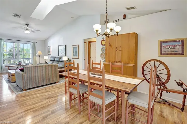 Dining space featuring light wood-type flooring, vaulted ceiling with skylight, and ceiling fan with notable chandelier