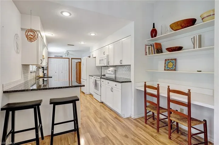 Kitchen with a kitchen bar, light wood-style flooring, white cabinets, white appliances, and a ceiling fan