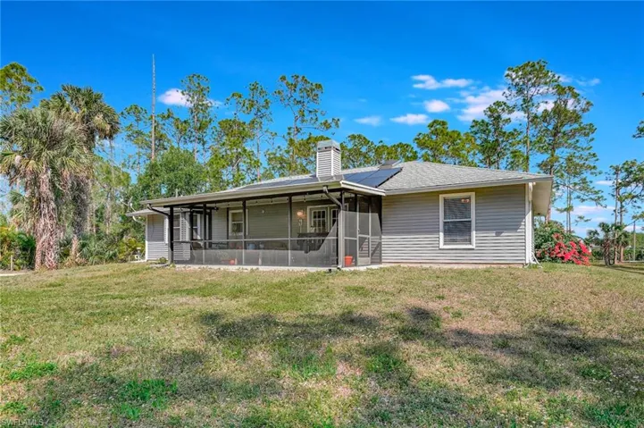 Back of property featuring a yard, roof mounted solar panels, chimney, and screened lanai