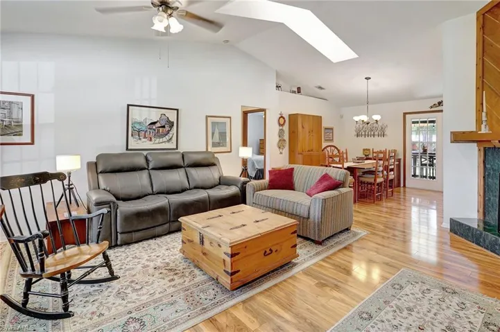 Living room with vaulted ceiling with skylight, ceiling fan with notable chandelier, and light wood-style floors
