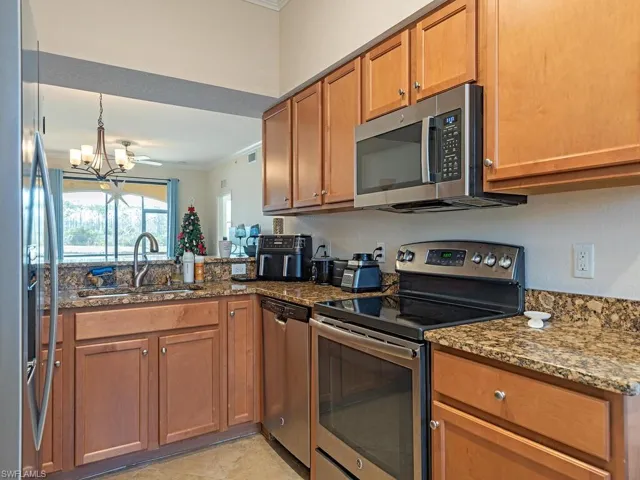 Kitchen featuring stainless steel appliances, crown molding, wood finish cabinetry, hanging lights, and dark stone countertops