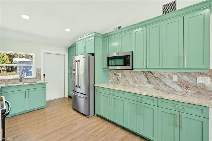 Kitchen featuring green cabinets, decorative backsplash, stainless steel appliances, recessed lighting, and light stone counters