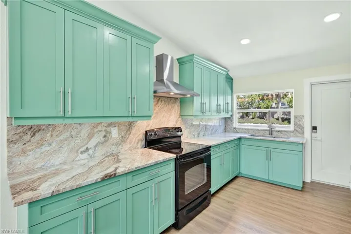 Kitchen featuring green cabinetry, black / electric stove, wall chimney exhaust hood, light stone counters, and recessed lighting
