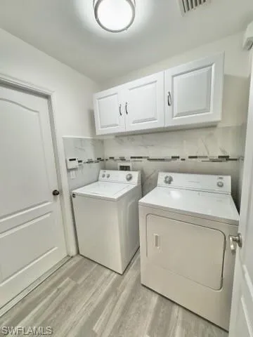 Washroom featuring washer and clothes dryer, light hardwood / wood-style floors, and cabinets