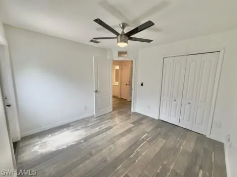 Unfurnished bedroom featuring a closet, dark wood-type flooring, and ceiling fan