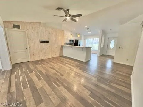 Unfurnished living room with ceiling fan, wood walls, lofted ceiling, and dark hardwood / wood-style flooring