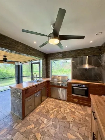 Kitchen with wall chimney range hood, sink, butcher block counters, stainless steel oven, and ceiling fan