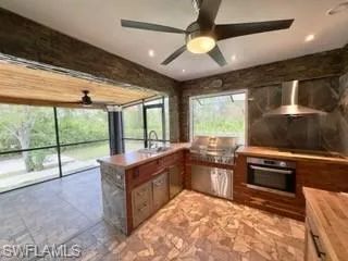 Kitchen featuring wooden counters, oven, wall chimney exhaust hood, kitchen peninsula, and sink