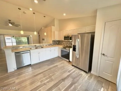 Kitchen with lofted ceiling, hanging light fixtures, light wood-type flooring, white cabinetry, and appliances with stainless steel finishes
