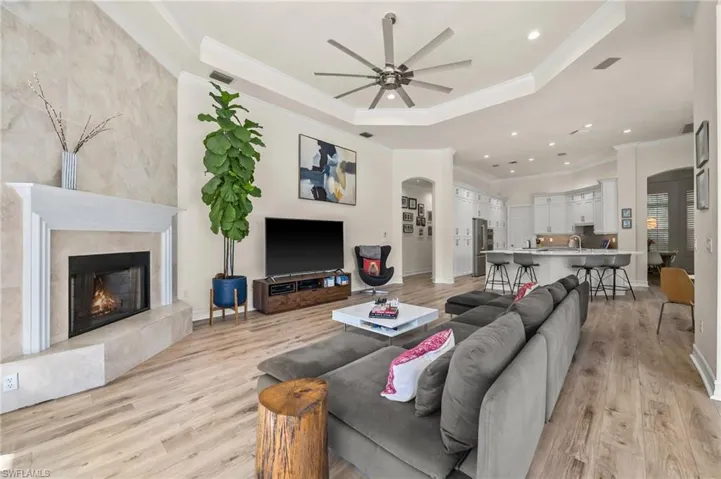 Living room featuring a fireplace, ornamental molding, ceiling fan, a raised ceiling, and light hardwood / wood-style flooring