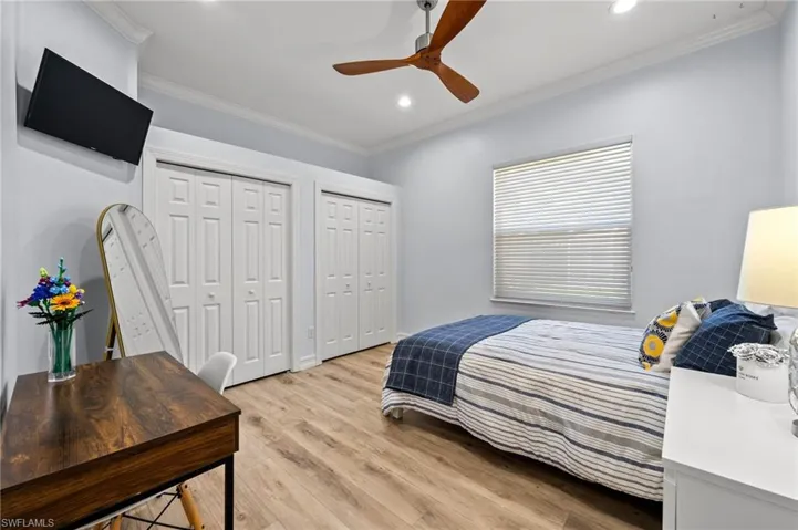 Bedroom with ornamental molding, two closets, ceiling fan, and light wood-type flooring