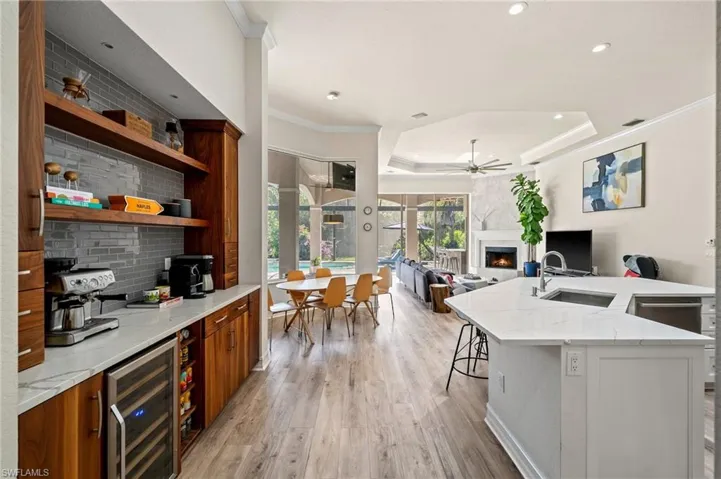 Kitchen featuring a fireplace, wine cooler, a kitchen bar, light stone countertops, and a center island with sink