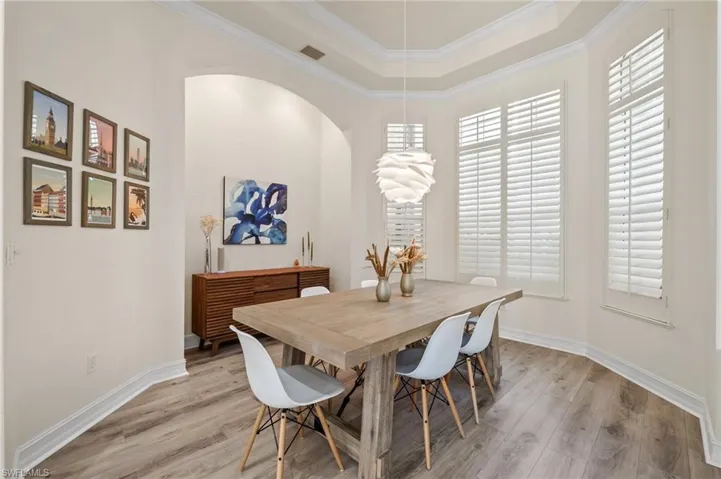 Dining space with a tray ceiling, light hardwood / wood-style flooring, and ornamental molding