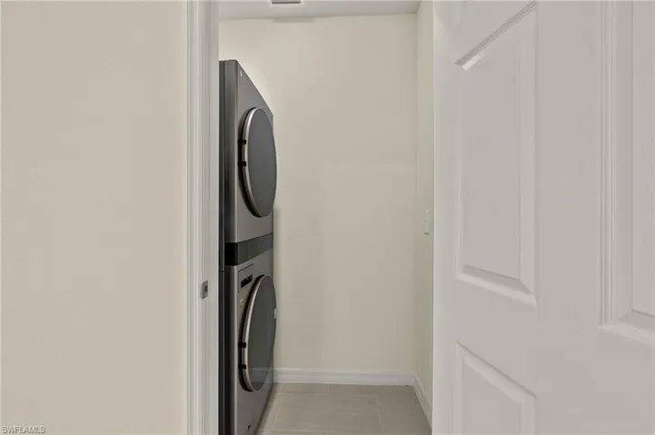 Washroom with stacked washing maching and dryer and light tile patterned flooring