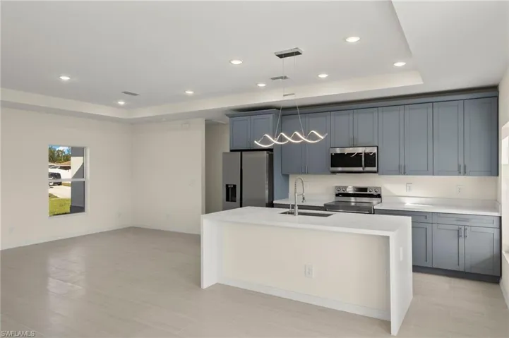 Kitchen with sink, appliances with stainless steel finishes, a raised ceiling, and an island with sink