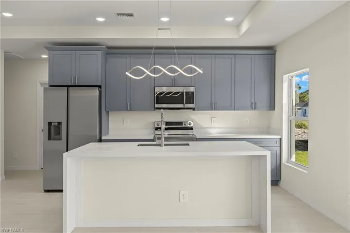 Kitchen with light stone countertops, appliances with stainless steel finishes, an island with sink, sink, and gray cabinets