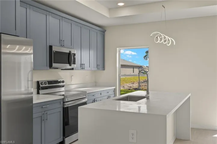 Kitchen featuring decorative light fixtures, sink, a kitchen island with sink, stainless steel appliances, and light stone counters