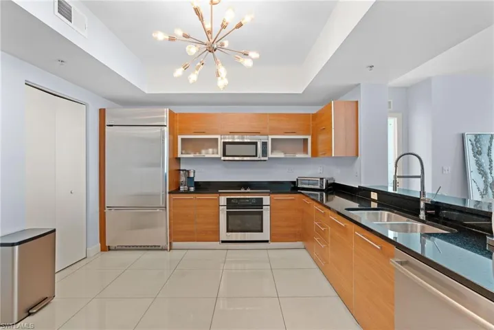 Kitchen featuring dark stone counters, stainless steel appliances, wood finish cabinetry, a tray ceiling, and modern cabinets