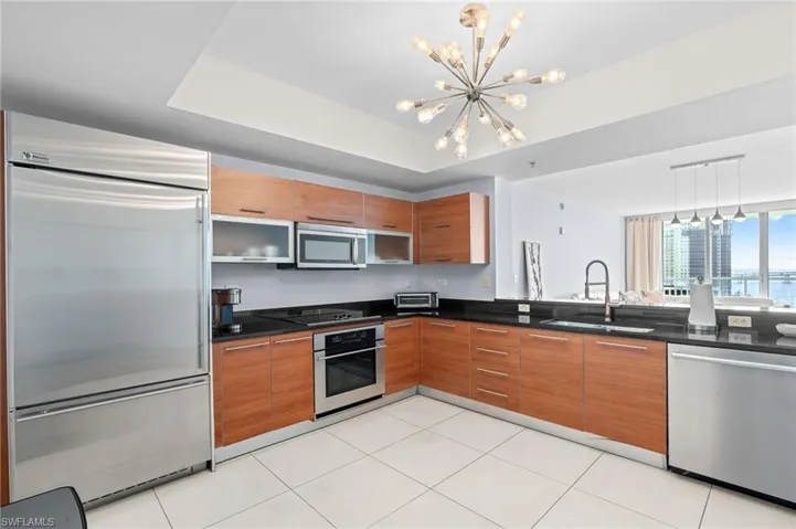 Kitchen with stainless steel appliances, wood finish cabinets, dark stone countertops, suspended lighting, and a raised ceiling