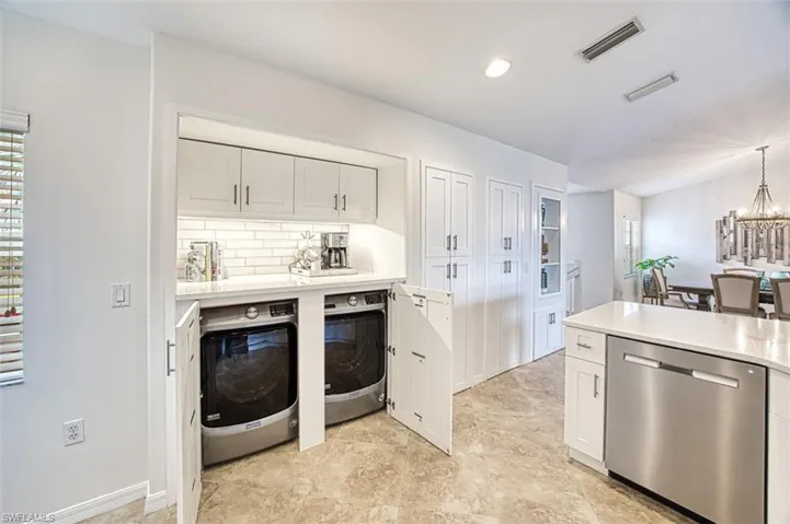 Kitchen featuring white cabinets, stainless steel dishwasher, decorative backsplash, light stone countertops, and hanging light fixtures