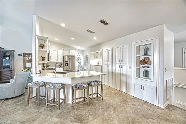 Kitchen featuring a breakfast bar area, a peninsula, white cabinets, open shelves, and light stone countertops