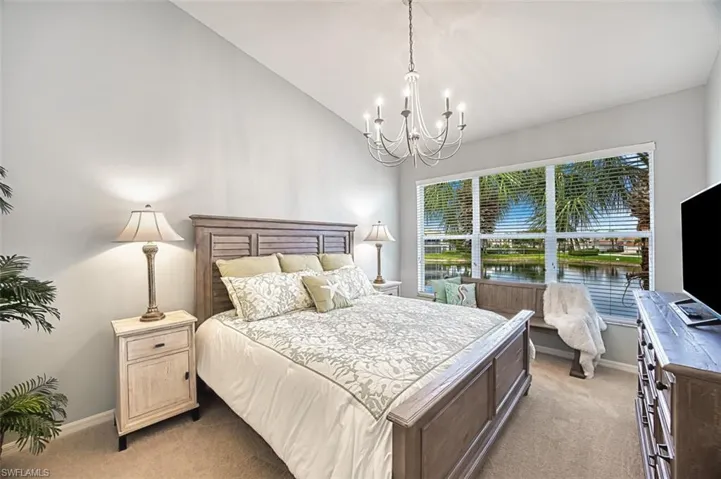 Bedroom with light colored carpet, lofted ceiling, and a chandelier