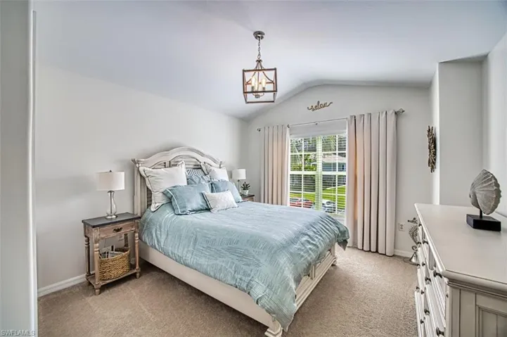 Bedroom with vaulted ceiling, light colored carpet, and a chandelier