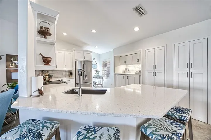 Kitchen featuring backsplash, a breakfast bar area, white cabinetry, light stone countertops, and a peninsula