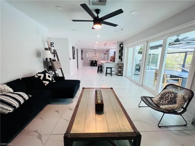 Living area with a ceiling fan, healthy amount of natural light, light marble finish flooring, and recessed lighting