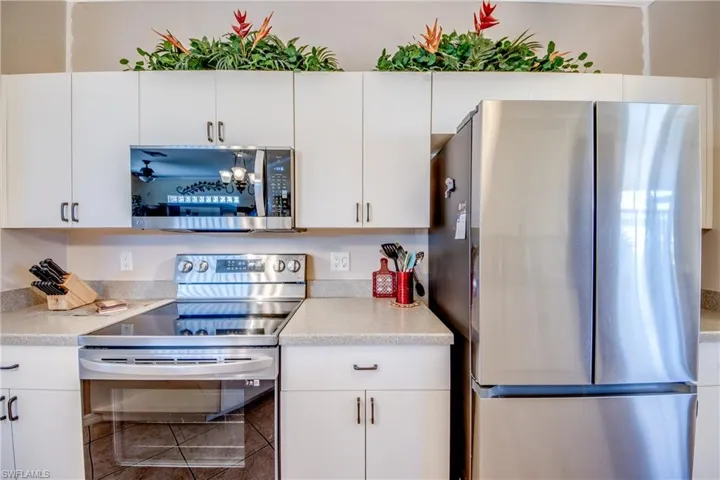 Kitchen featuring white cabinetry, solid-surface countertops, and stainless steel appliances including a built-in microwave, range, and French-door refrigerator