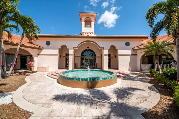 Exterior facade featuring a central cupola, tiled roof, arched architectural details, and a circular fountain with teal tile inlay set in a paved courtyard