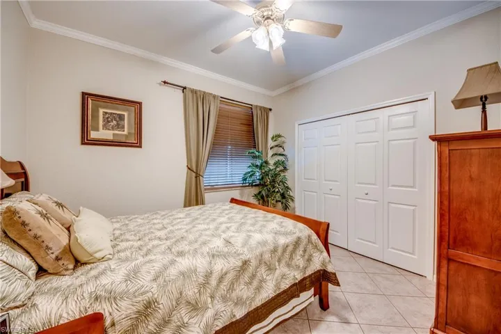 Neutral-toned room featuring tile flooring, crown molding, a central ceiling fan with multi-light fixture, and double-door closet cabinetry