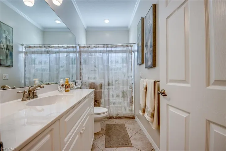 Full-width vanity with a light-toned countertop, integrated basin, brushed metal faucet, large wall-mounted mirror, and tile flooring