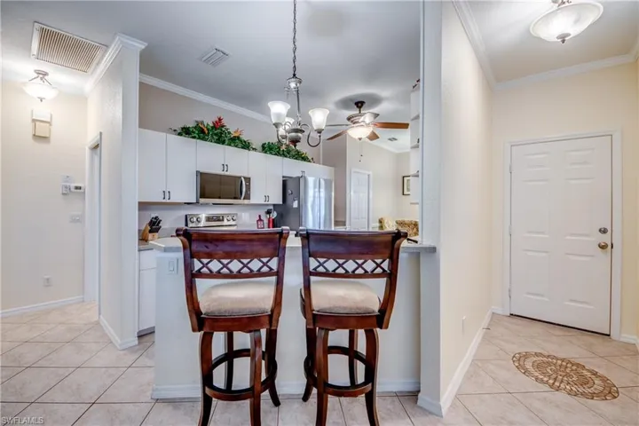 Kitchen featuring white cabinetry, stainless steel appliances, stone-surfaced breakfast bar, and pendant lighting