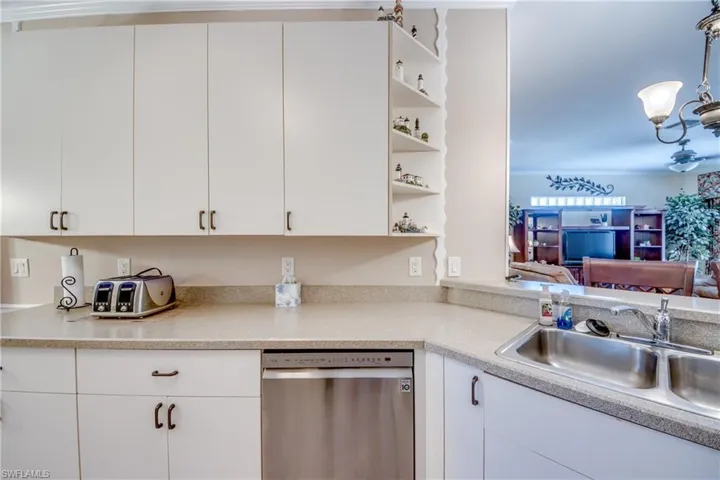 Kitchen featuring white cabinetry, integrated corner shelving, solid-surface countertops, and a stainless steel dishwasher