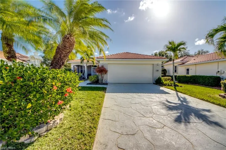 Single-story exterior featuring a tile roof, decorative stamped concrete driveway, two-car garage, and mature palm landscaping