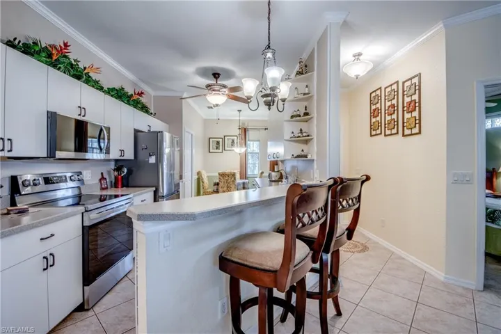 Kitchen featuring white cabinetry, stainless steel appliances, tile flooring, a breakfast bar with stone-finish countertops, and decorative built-in corner shelving