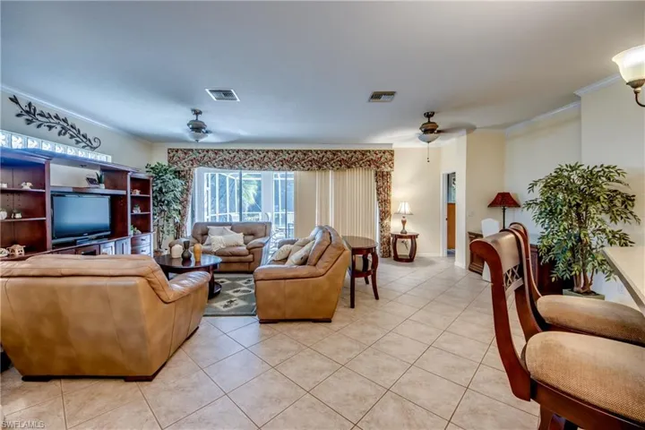 Open-concept living space featuring large-format ceramic tile flooring, built-in wooden media cabinetry with glass shelving, recessed ceiling lighting, and sliding glass doors