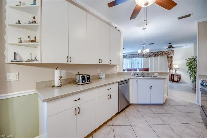 Kitchen featuring white shaker-style cabinetry, open corner shelving, solid-surface countertops, a stainless steel dishwasher, and tile flooring