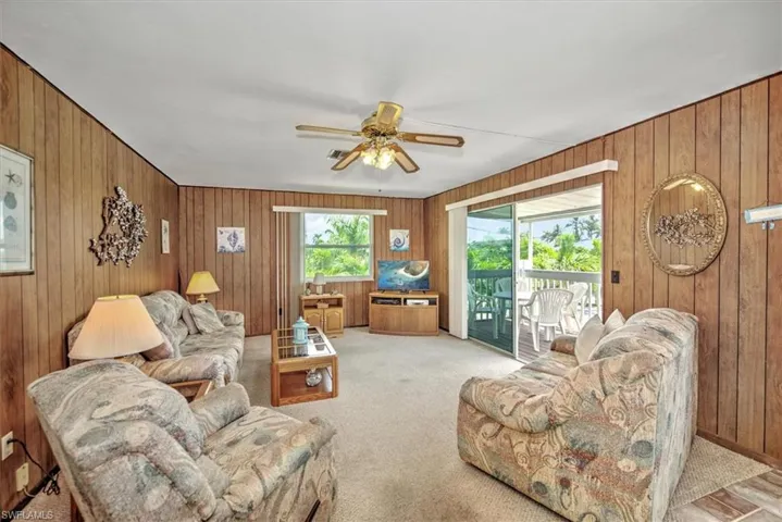 Carpeted living room featuring ceiling fan and wooden walls