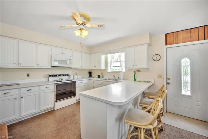 Kitchen with white cabinetry, white appliances, a breakfast bar, and kitchen peninsula