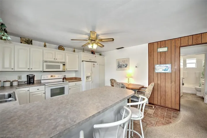 Kitchen featuring white cabinetry, a kitchen bar, white appliances, and wood walls