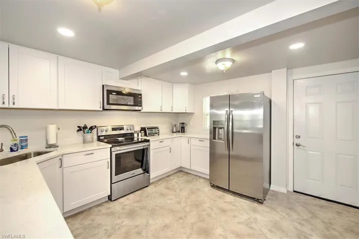 Kitchen with white cabinetry, sink, light stone counters, and stainless steel appliances