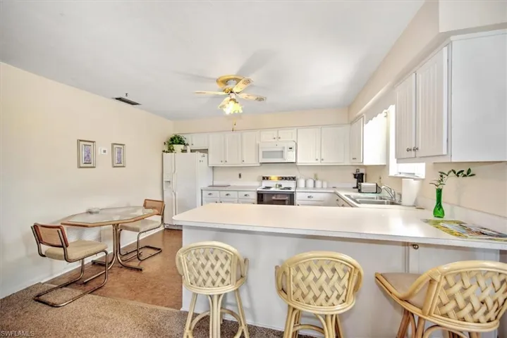 Kitchen featuring white cabinetry, white appliances, a breakfast bar area, and kitchen peninsula