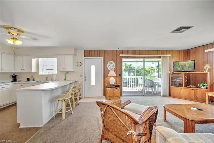 Carpeted living room featuring sink, ceiling fan, and wood walls