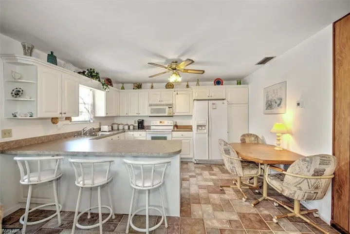 Kitchen featuring white cabinetry, sink, white appliances, and a breakfast bar area