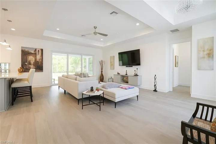 Living room featuring a raised ceiling, light wood-style floors, recessed lighting, and a ceiling fan